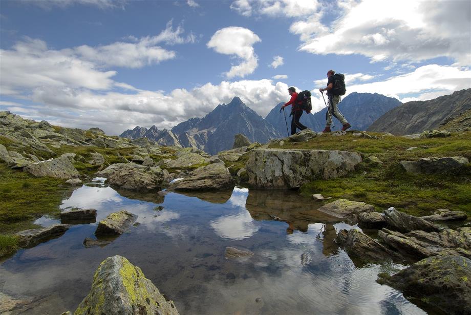 Two hikers with a little pond in the front and with the mountain called Bretterkopf in the background
